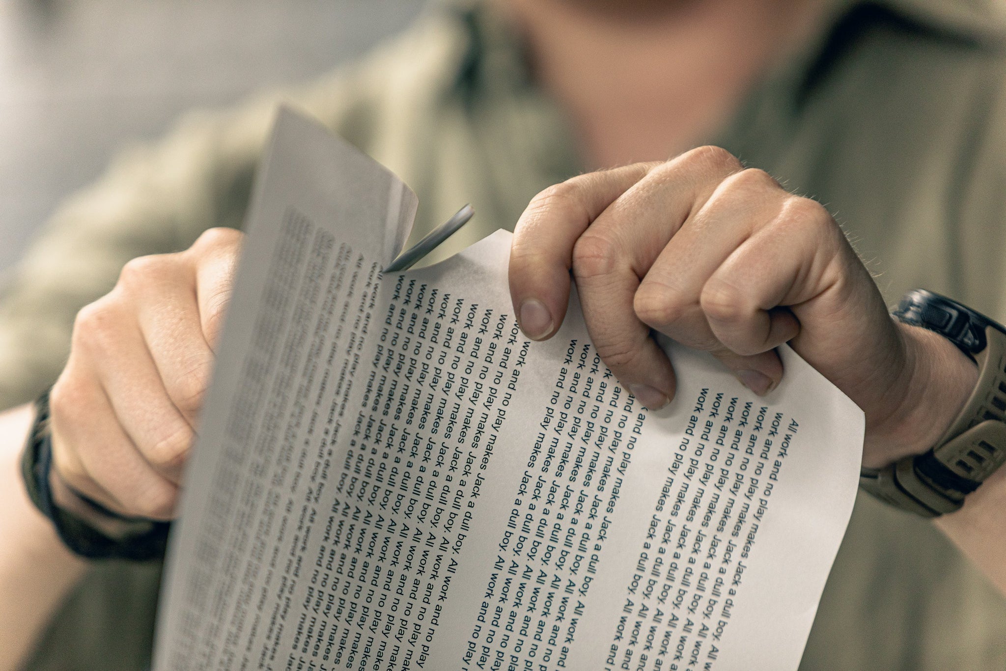Man holding a paper full of "All work and no play makes Jack a dull boy" quotes, and cuts the paper with Varusteleka Jääkäripuukko 110