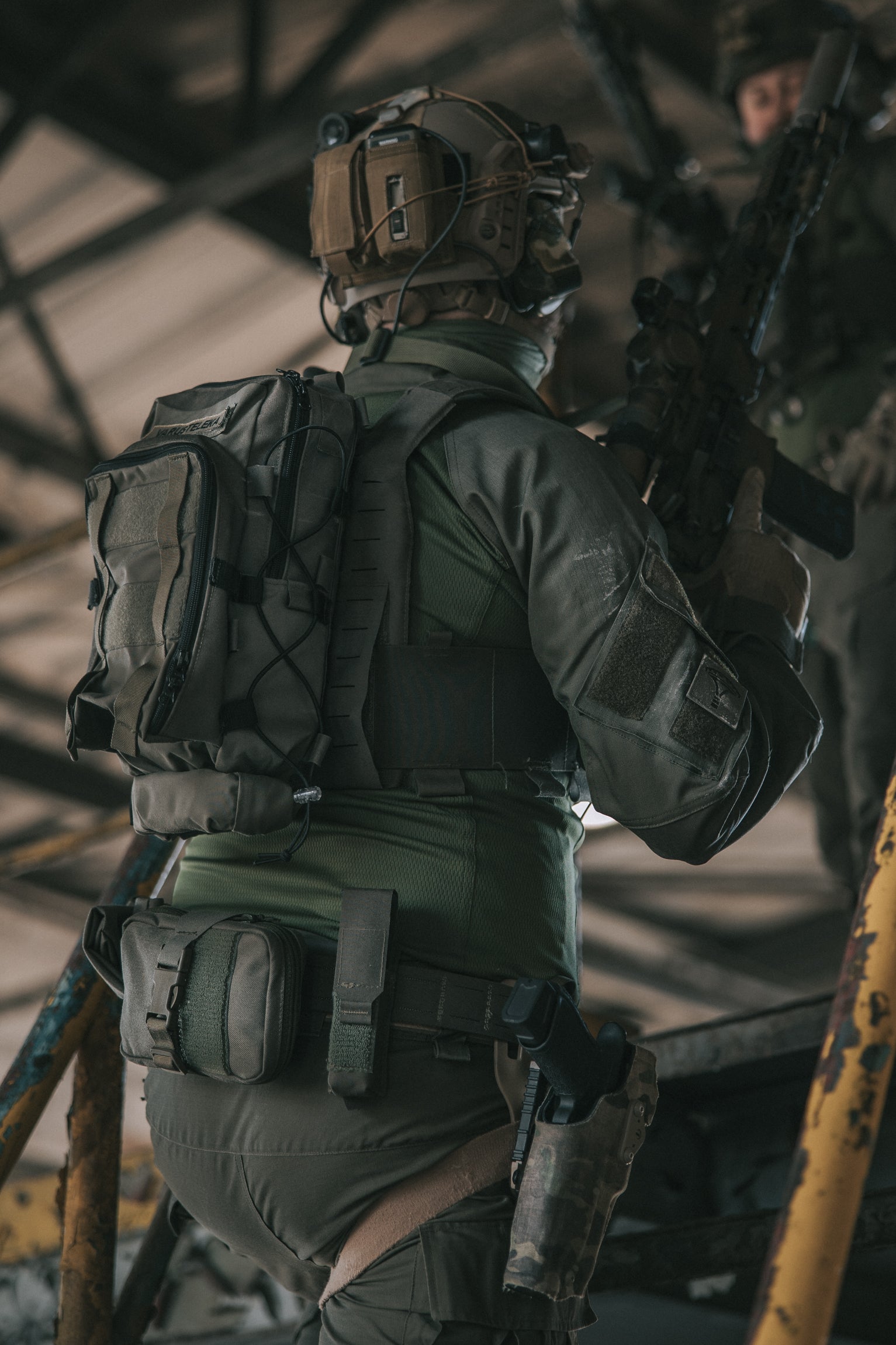 Person in tactical gear with a backpack and rifle in an industrial setting