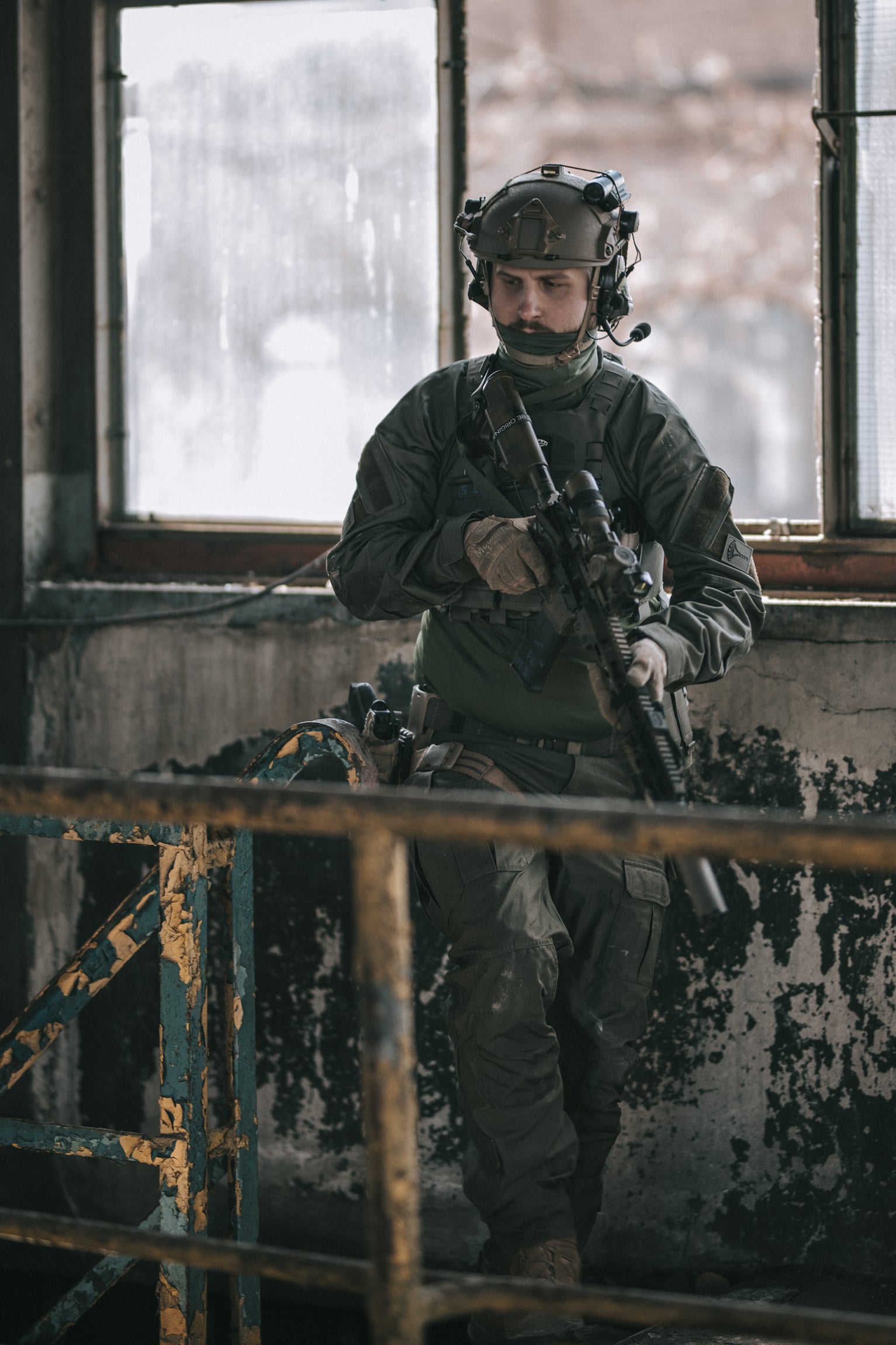 Person in military gear holding a rifle inside a dilapidated building.