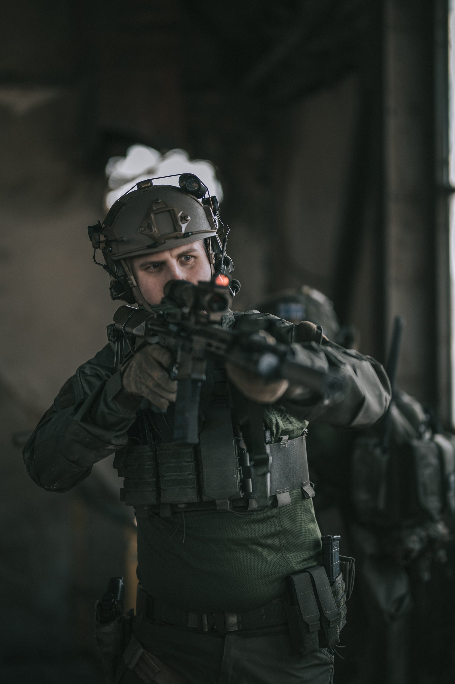 Person in tactical gear aiming a rifle with a dark background