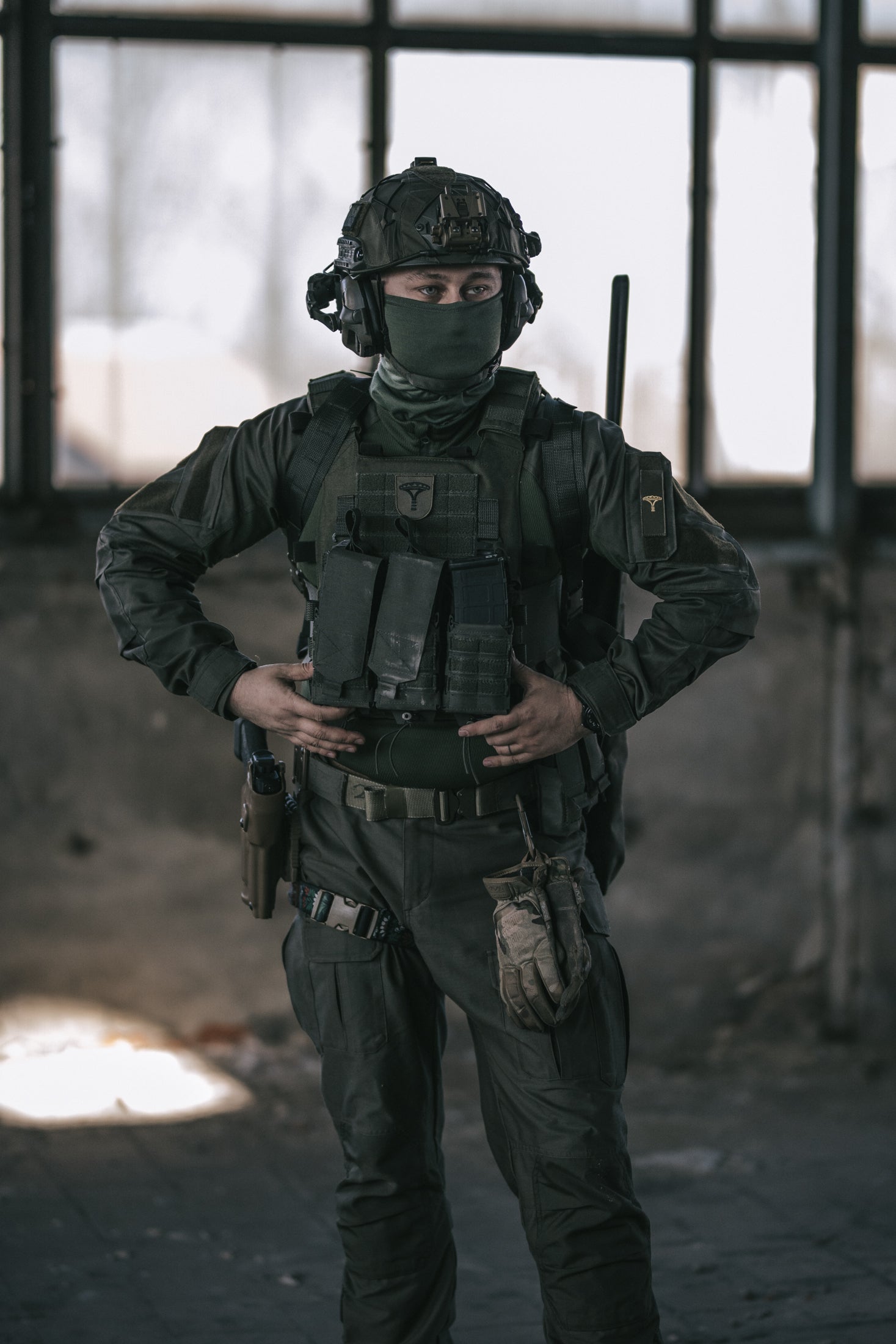 Person in tactical gear standing in a dimly lit room with large windows.