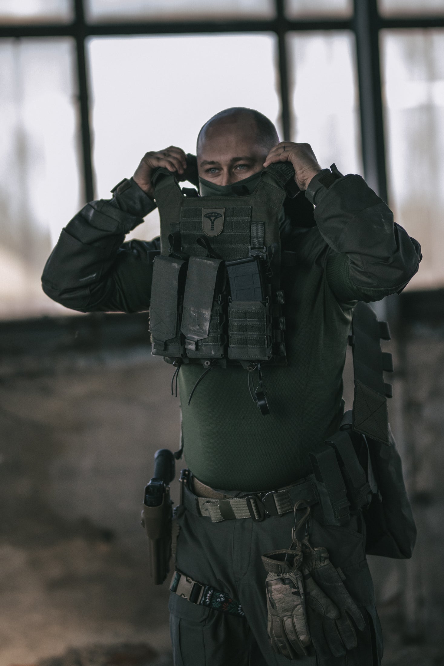 Person in tactical gear adjusting their mask in a dimly lit room.
