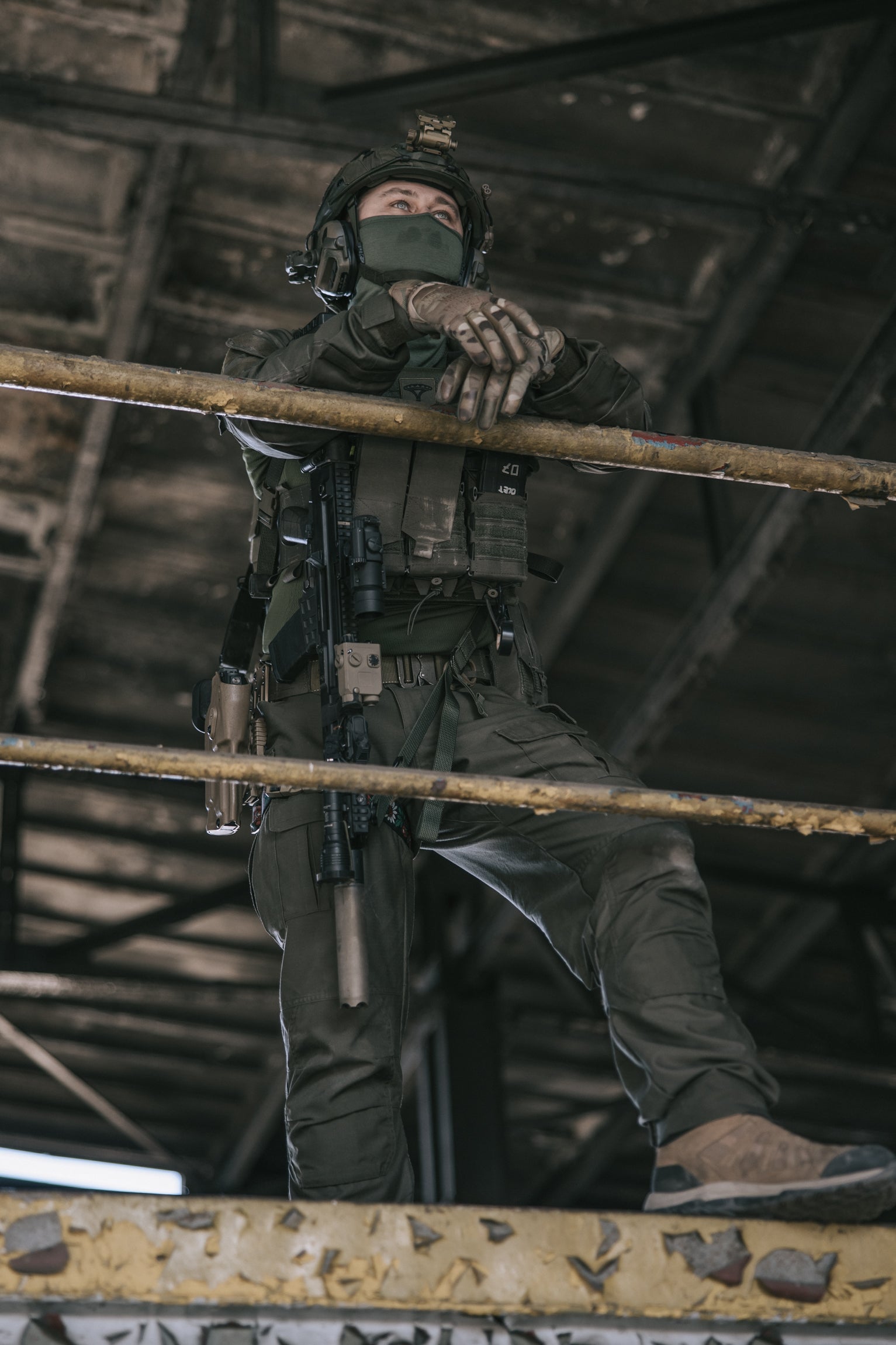 Person in tactical gear standing on a metal beam in an industrial setting