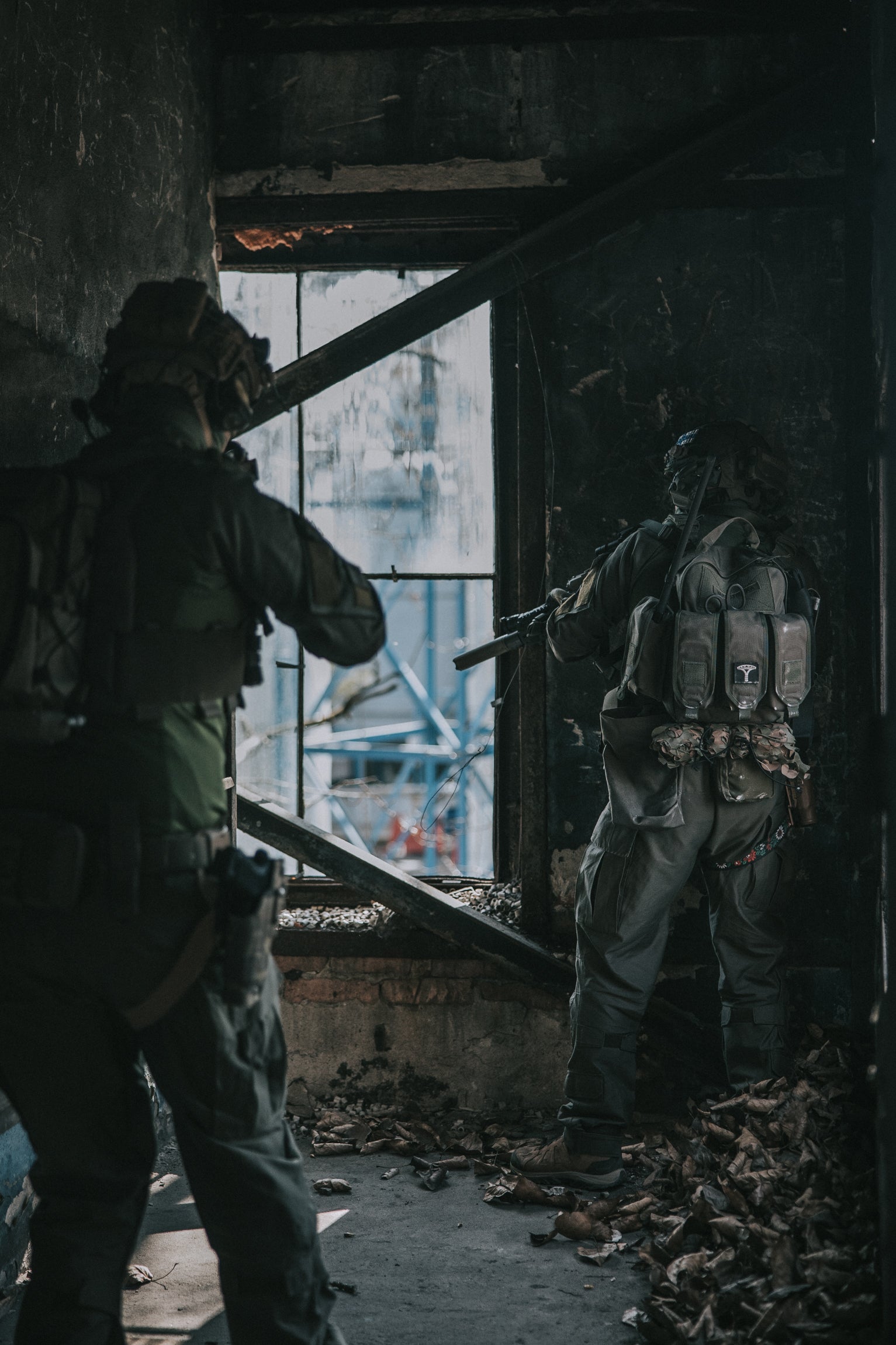 Two individuals in military or tactical gear in a dilapidated building.
