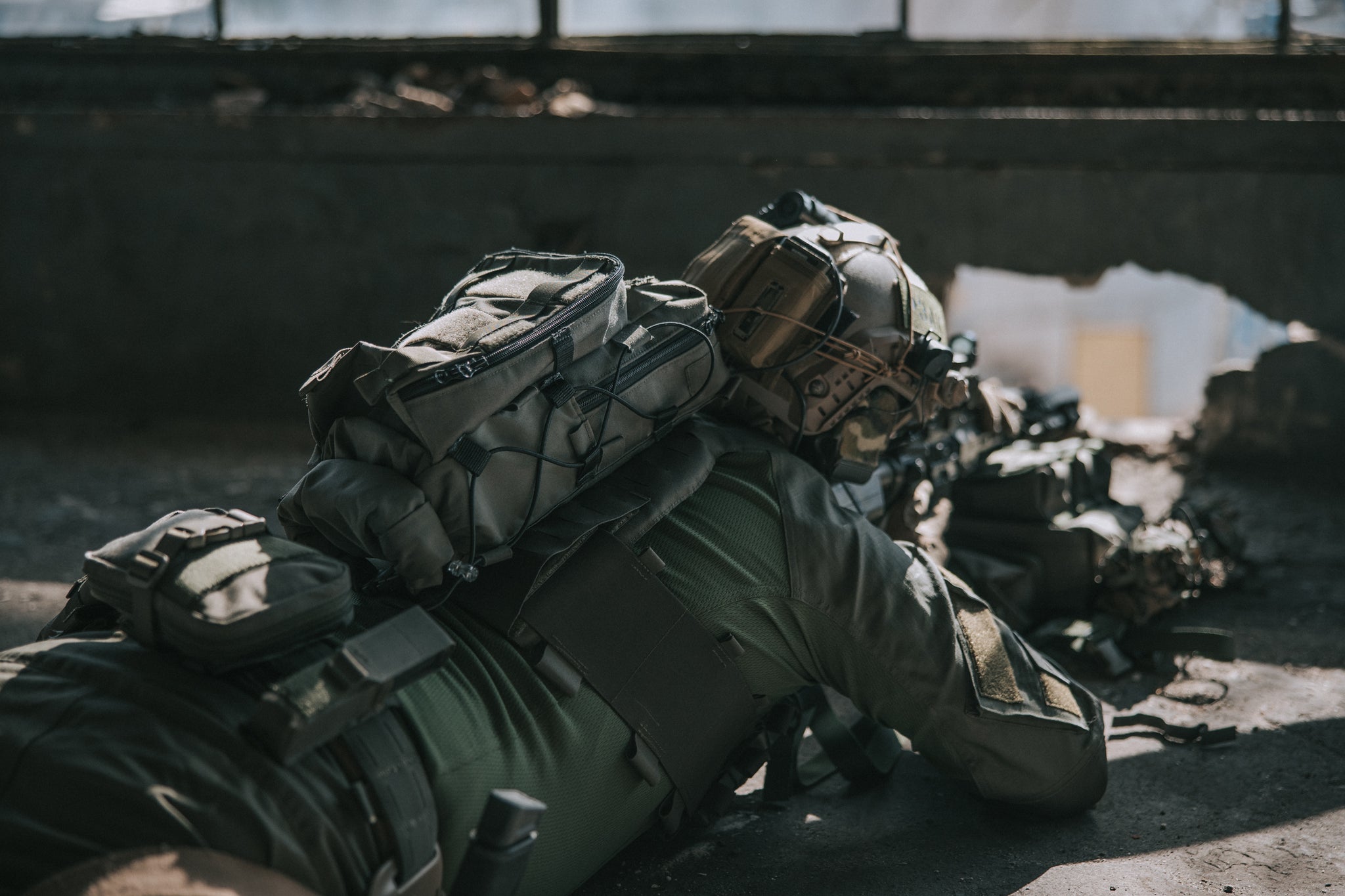 Person in military gear lying on the ground with a backpack