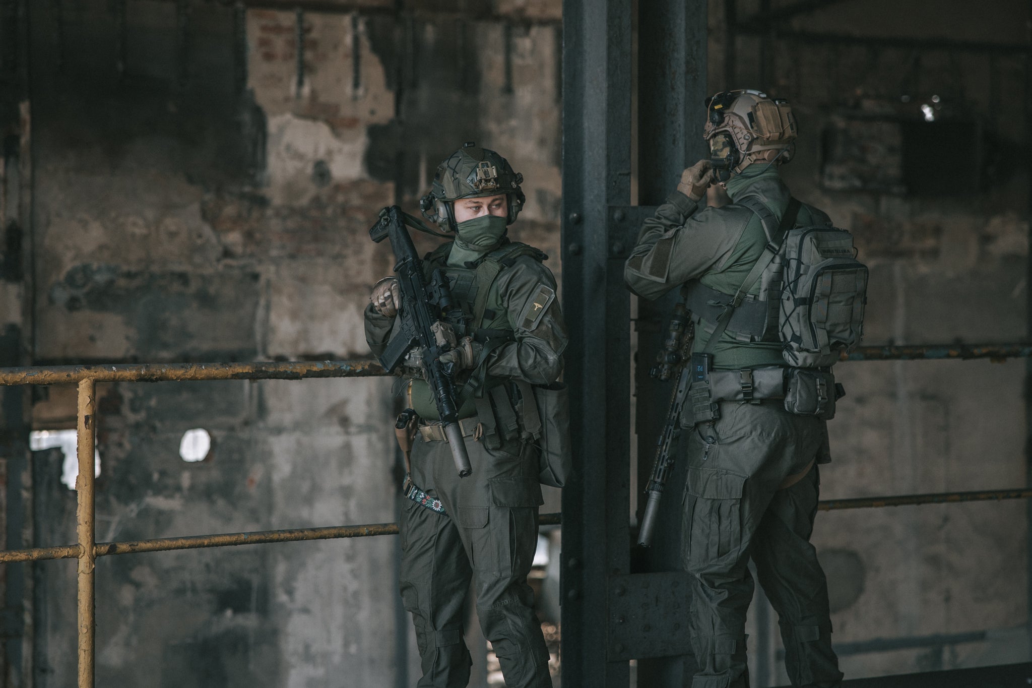 Two soldiers in tactical gear standing in a dimly lit industrial setting.
