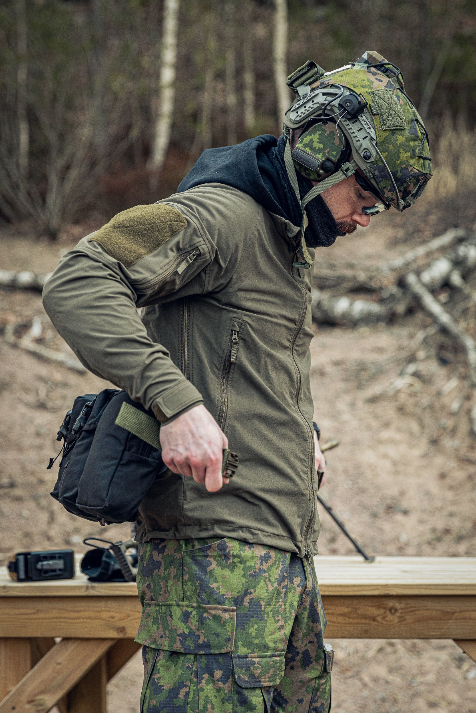 Person in military gear putting on a belt at a shooting range.