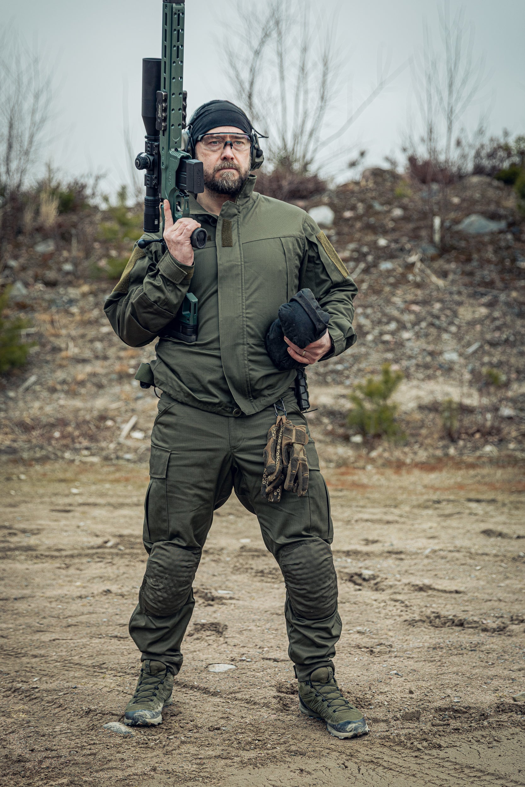 Man in tactical gear holding a rifle in an outdoor setting