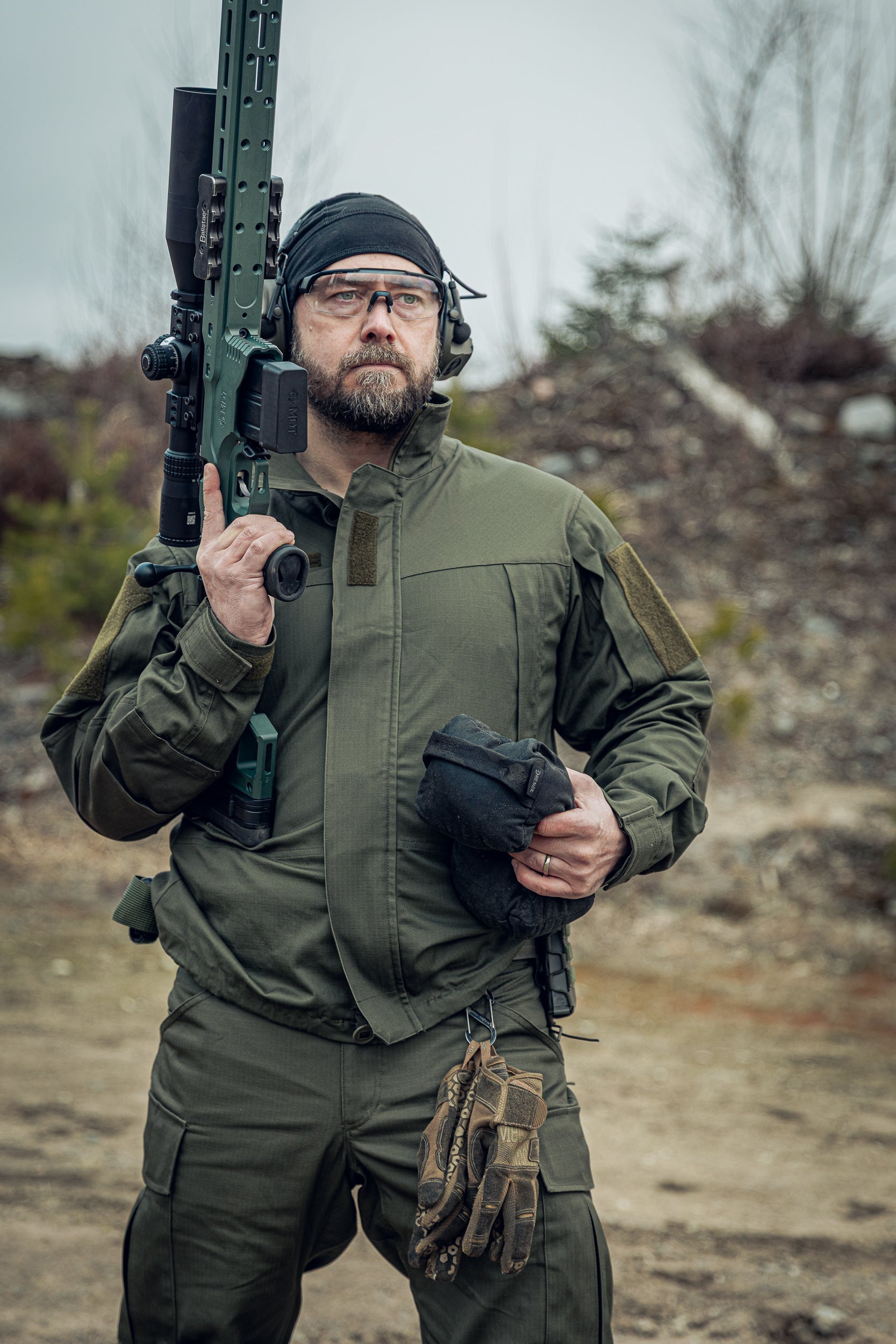 Person in tactical gear holding a rifle in an outdoor setting