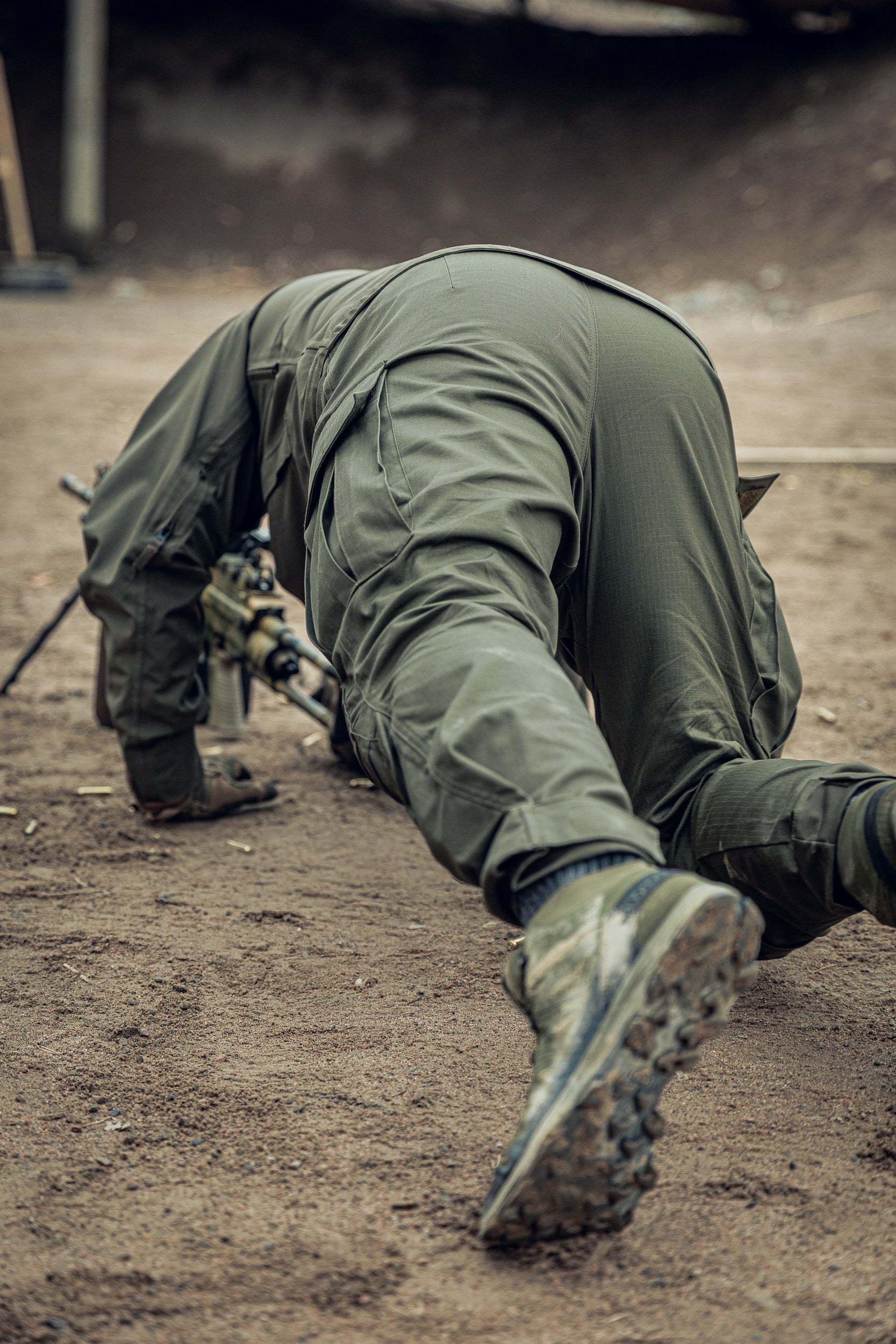 Person in military uniform crouching on a dirt ground