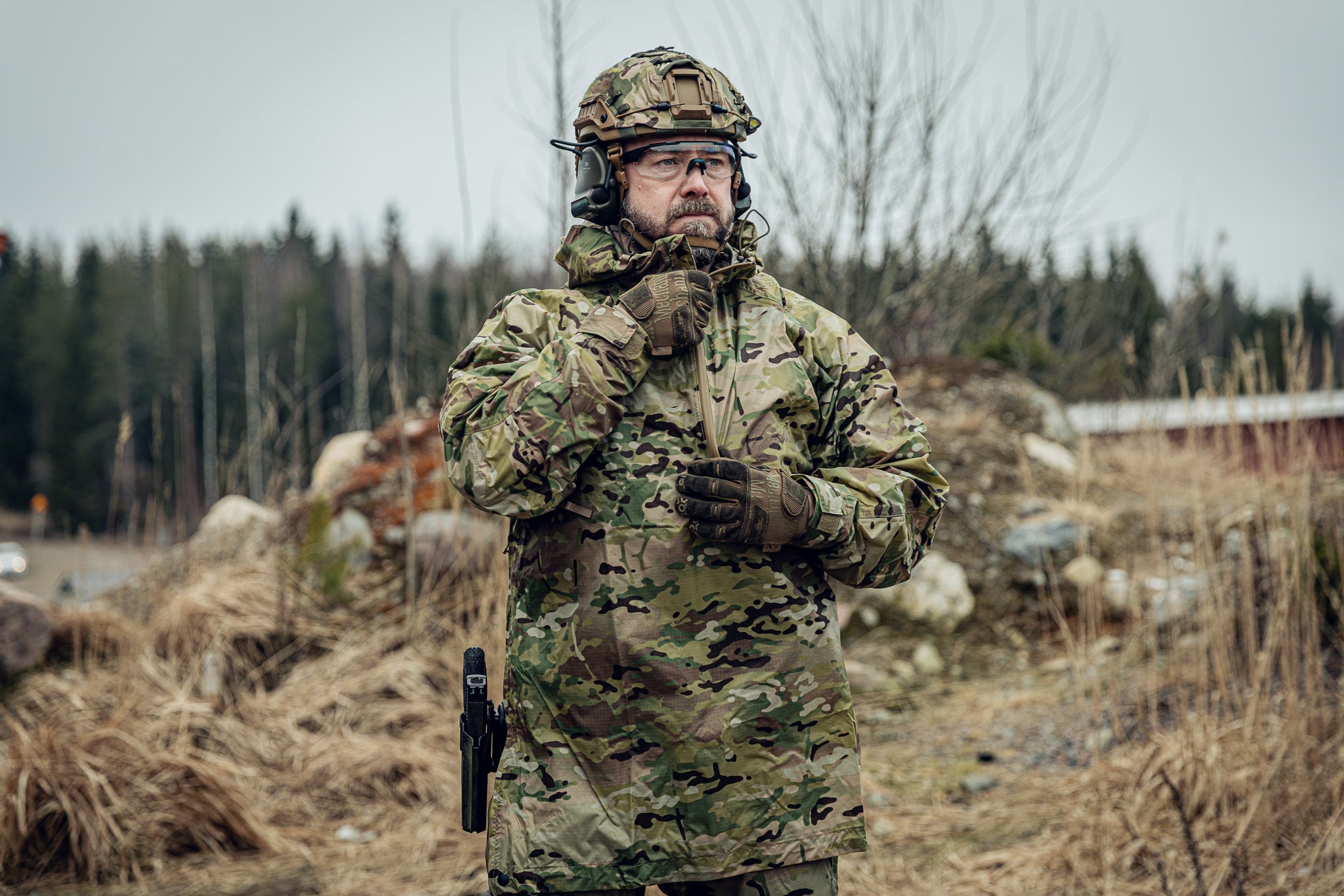 Person in full military gear standing in a natural setting with trees and rocks.