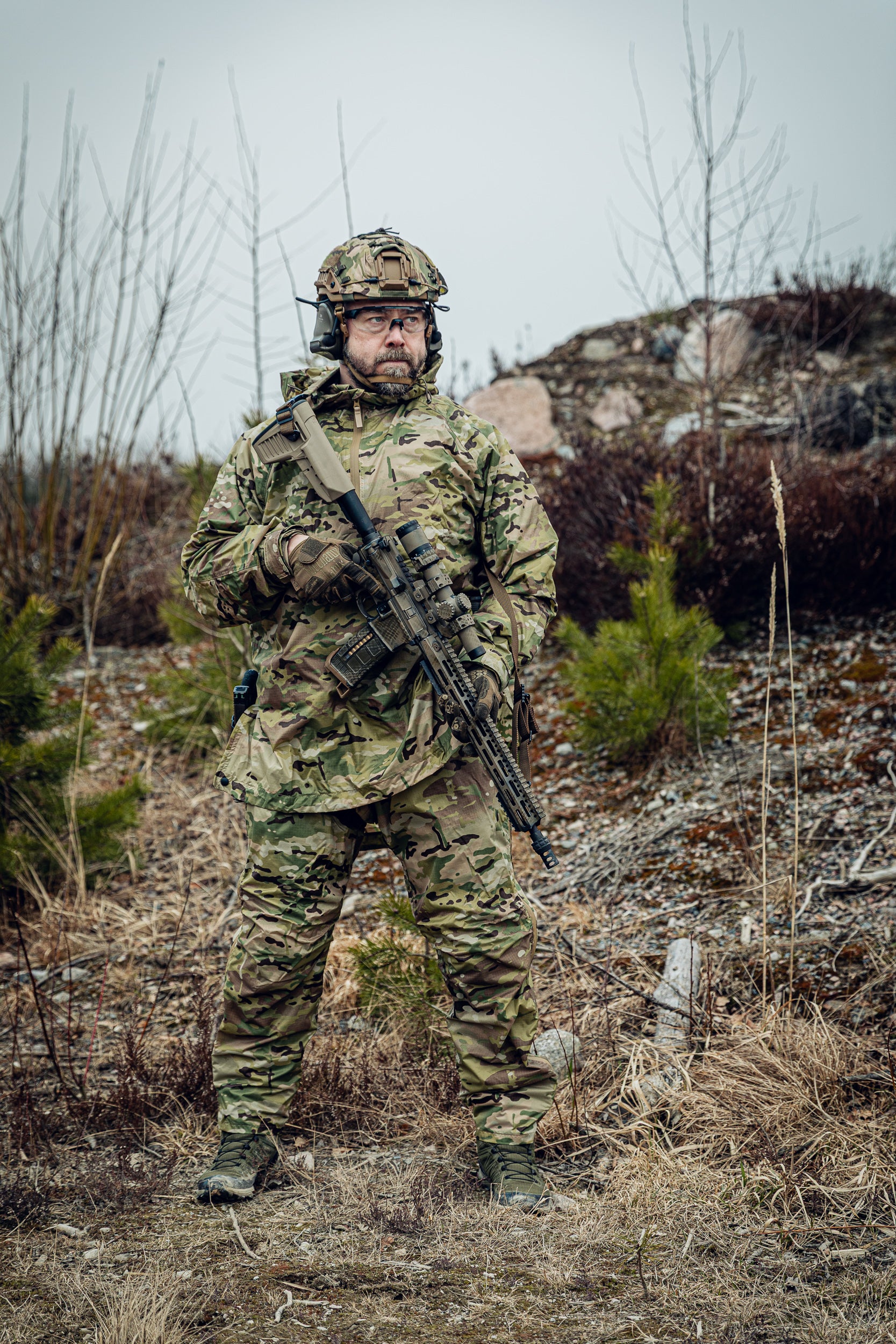 Person in camouflage military gear holding a rifle in a natural setting