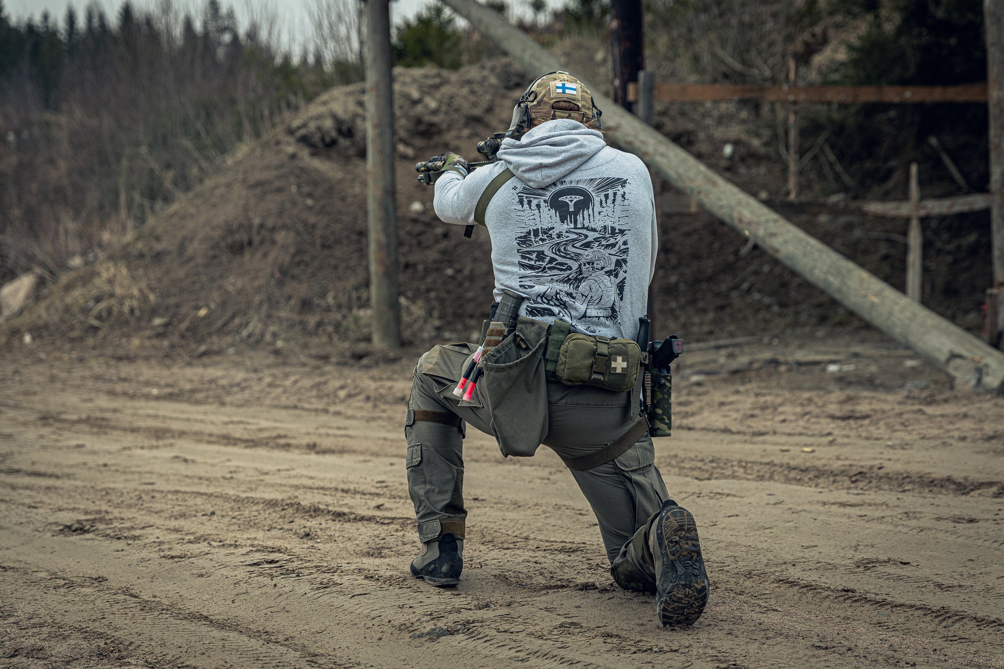 Person in tactical gear and a grey print hoodie at an outdoor shooting range.