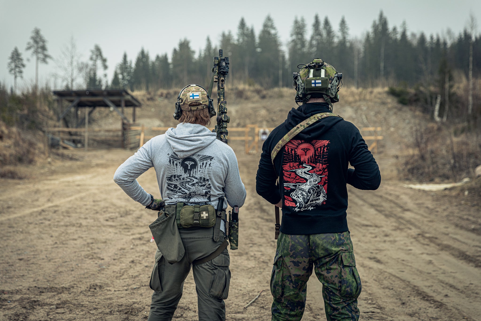 Two people in tactical gear and matching print hoodies at an outdoor shooting range.