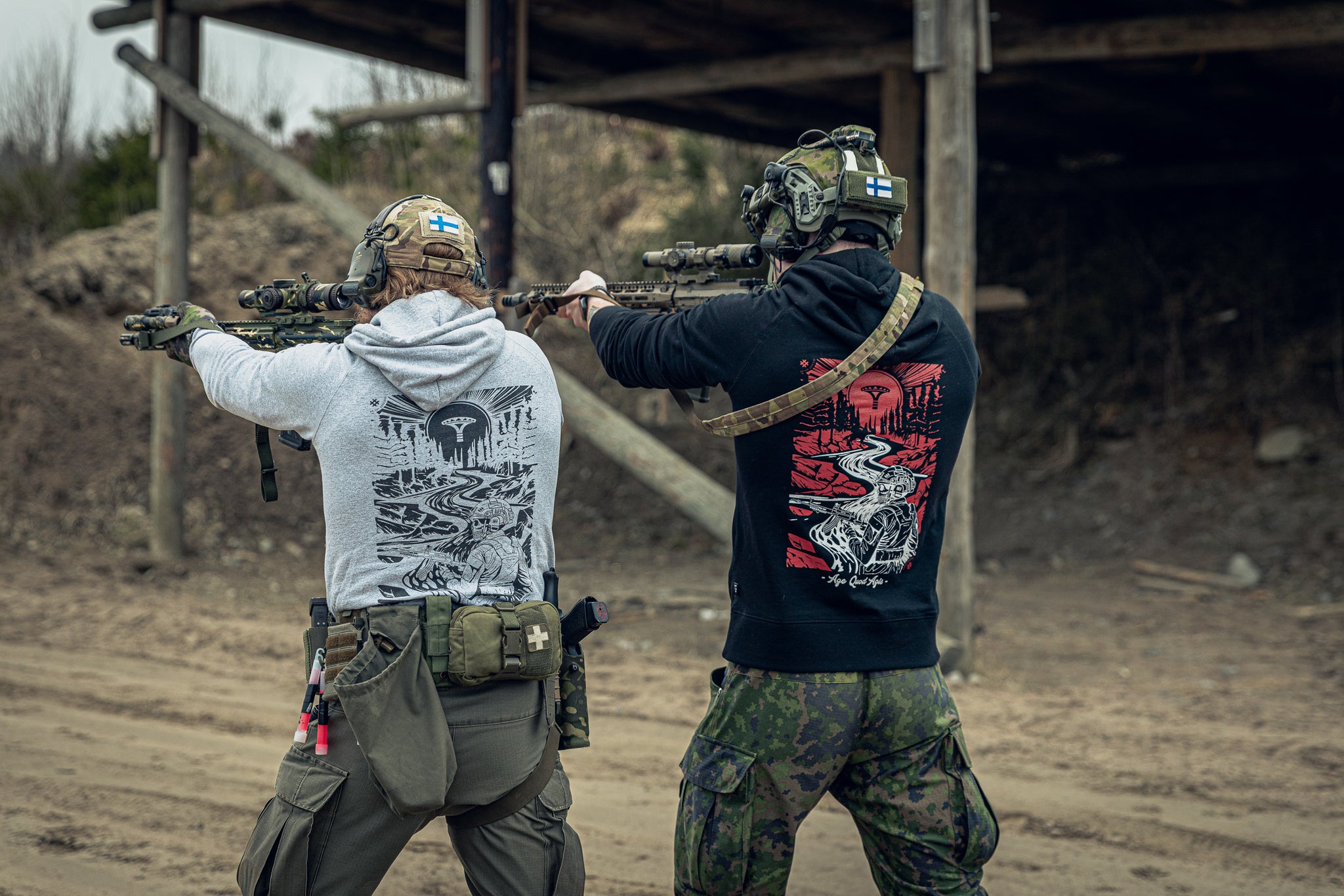 Two individuals in tactical gear and matching print hoodies at an outdoor shooting range.