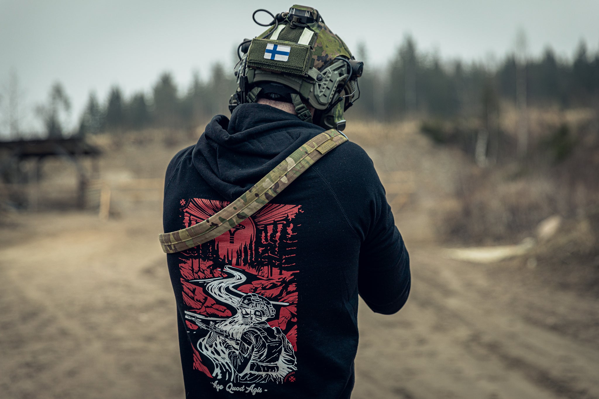 Person wearing a black hoodie with a red and white design at an outdoor shooting range.
