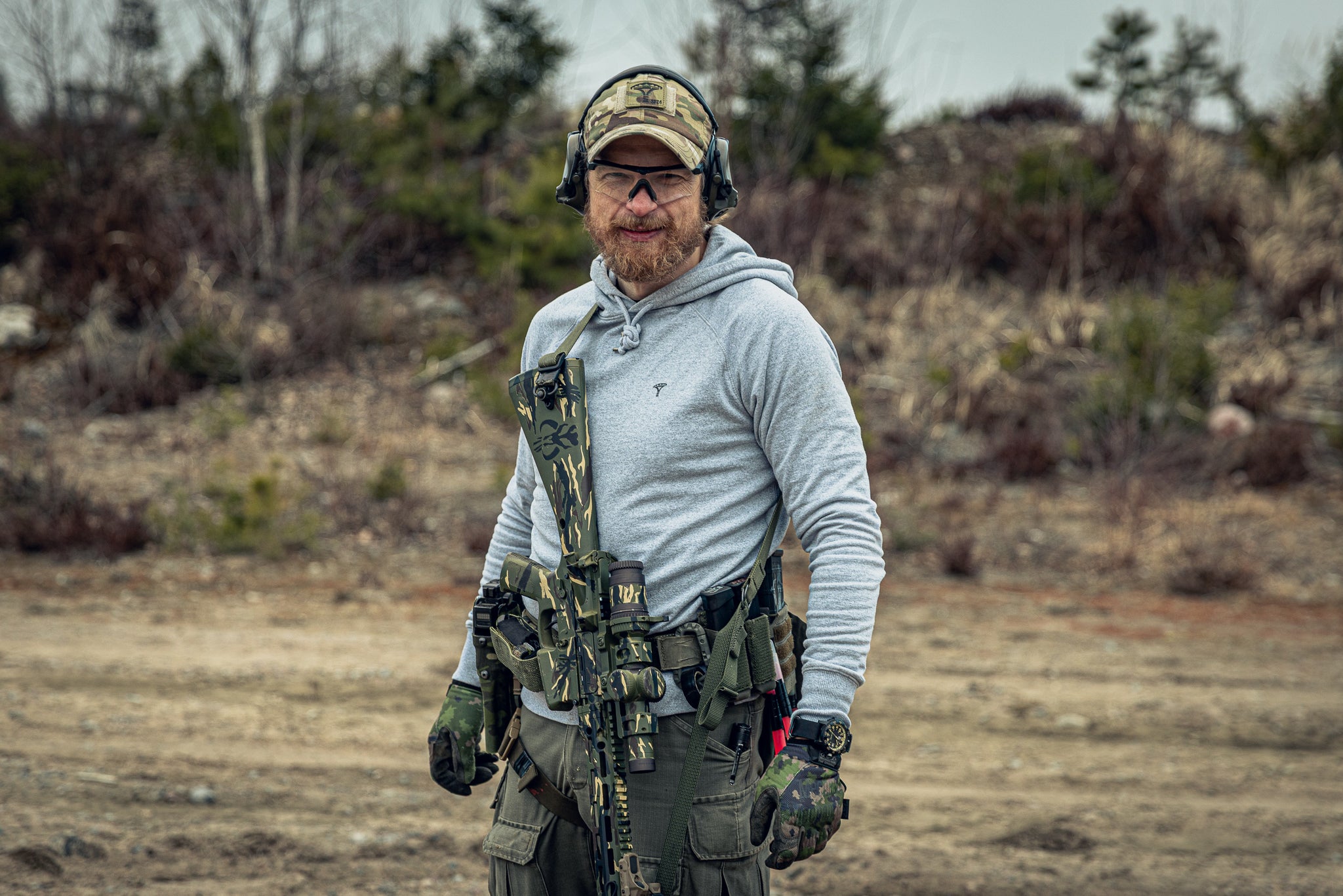 Person in tactical gear and a grey hoodie at an outdoor shooting range.