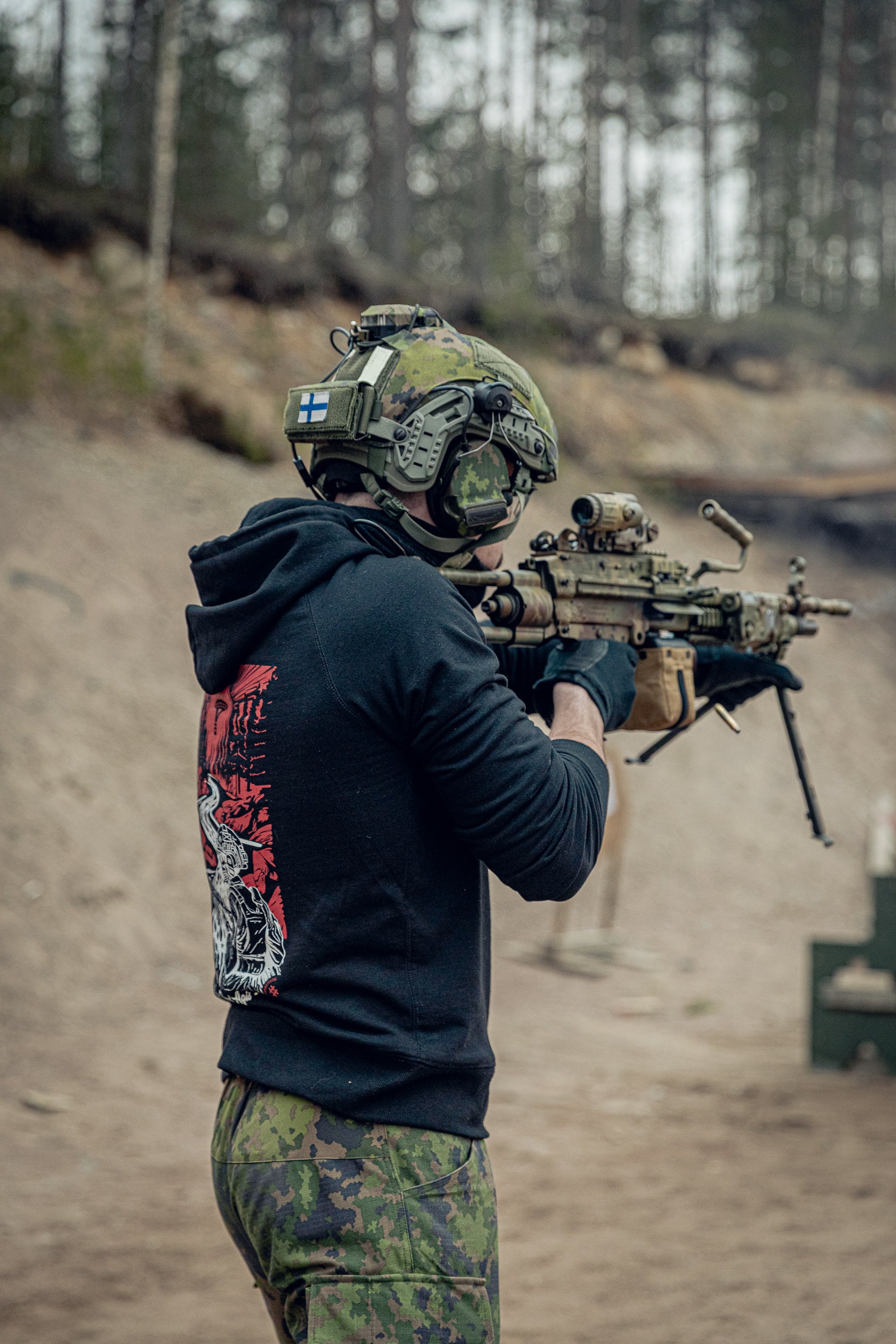 Person in tactical gear and a balck print hoodie holding a rifle at a shooting range.