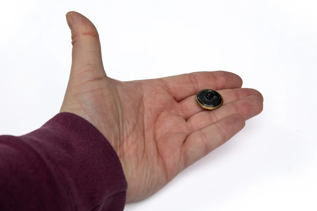 Large brass button. The backside is either black or metal-colored steel.